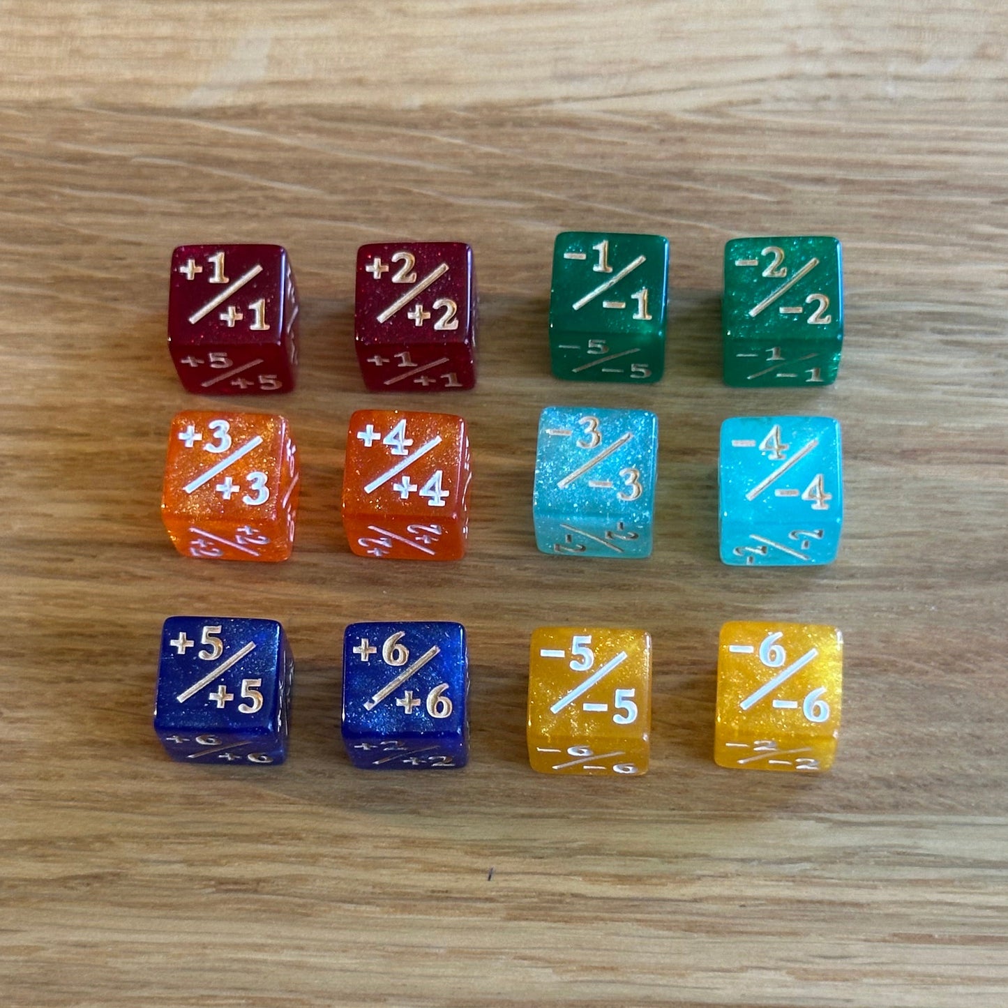 Set of 12, assorted 12mm six-sided counter dice, including six +/+ dice and six -/- dice, used for tracking game modifiers.