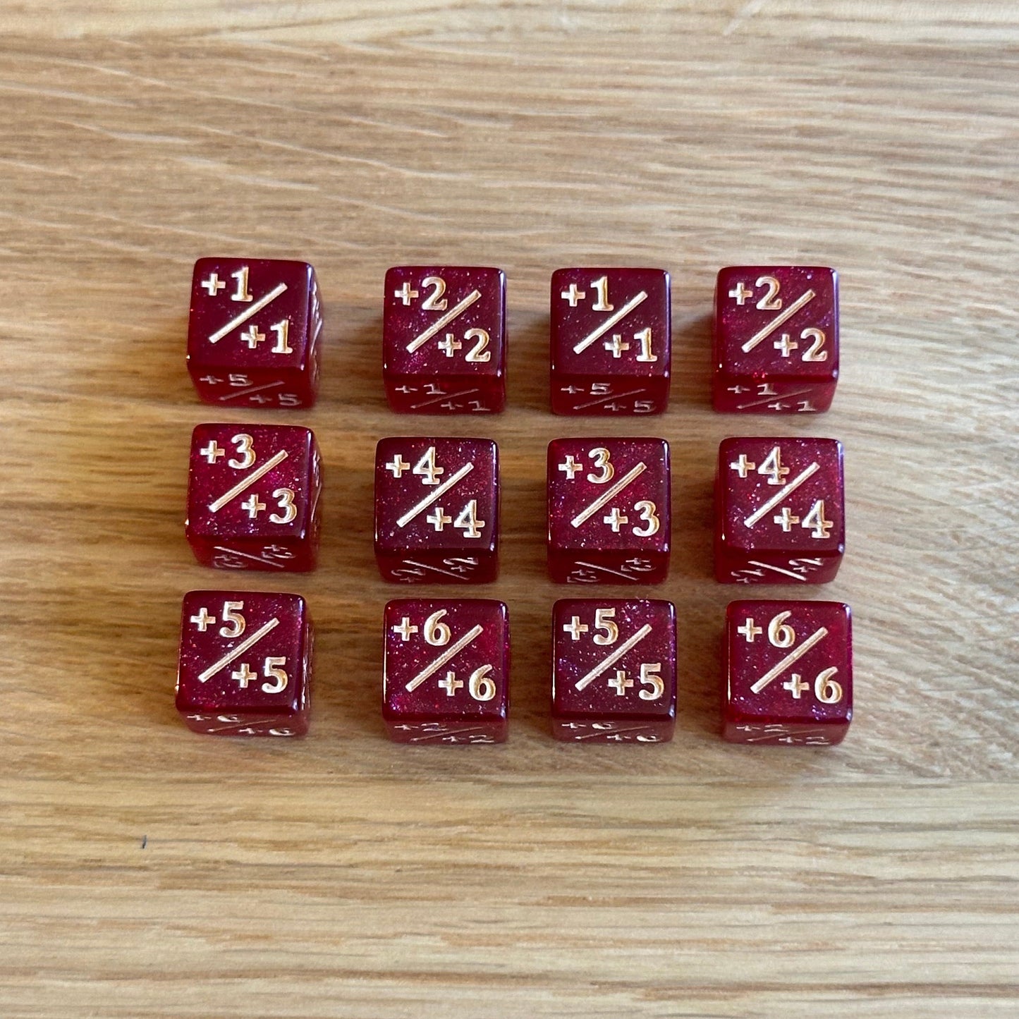Set of twelve 12mm D6 +/+ plus plus dice in glitter deep red with gold infill. each dice is numbered 1-6 on each side to track incremental positive modifiers.