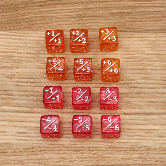 Set of 12, 12mm six-sided counter dice, including six orange glitter +/+ dice with white infill and six pink glitter -/- dice with white infill, used for tracking game modifiers.