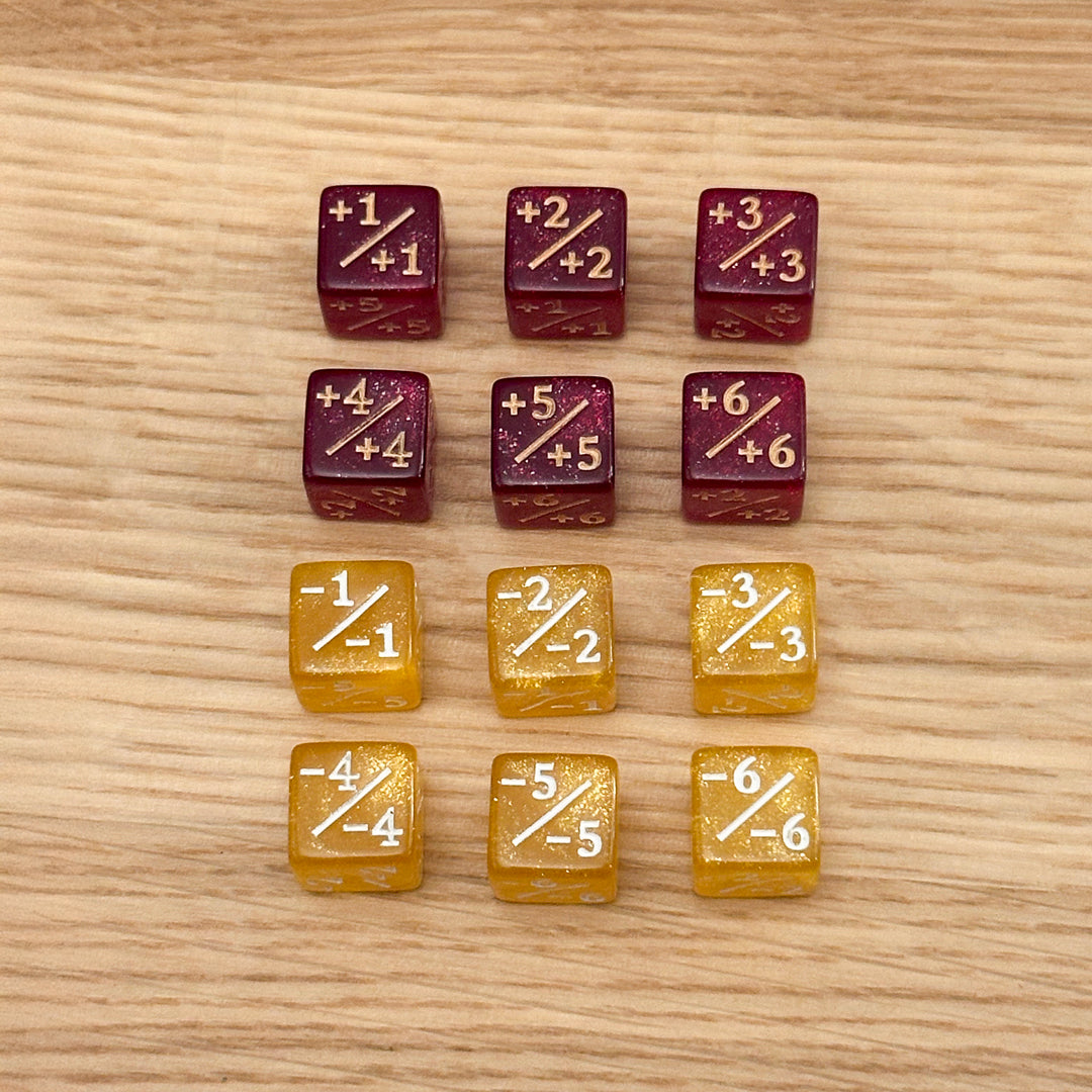 Set of 12, 12mm six-sided counter dice, including six deep red glitter +/+ dice with gold infill and six yellow glitter -/- dice with white infill, used for tracking game modifiers.