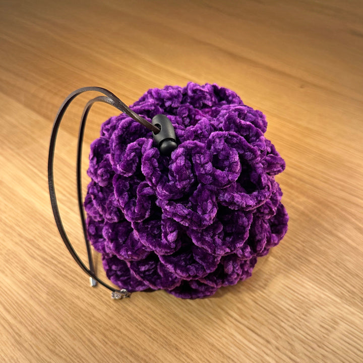 Crochet dragon egg dice bag made from purple velvet yarn with chocolate leather drawstring and black plastic toggle, shown closed.