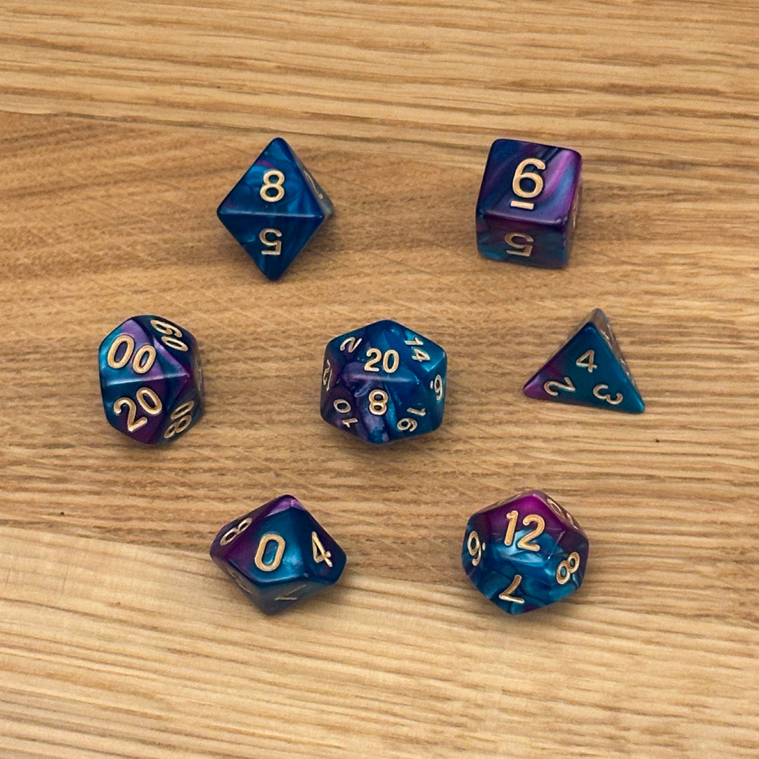 Set of 7 polyhedral dice (D4, D6, D8, D10, percentile D10, D12, D20) in swirled in galactic blue and purple acrylic with gold number infill.