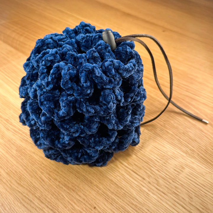 Crochet dragon egg dice bag made from navy velvet yarn with chocolate leather drawstring and black plastic toggle, shown closed.
