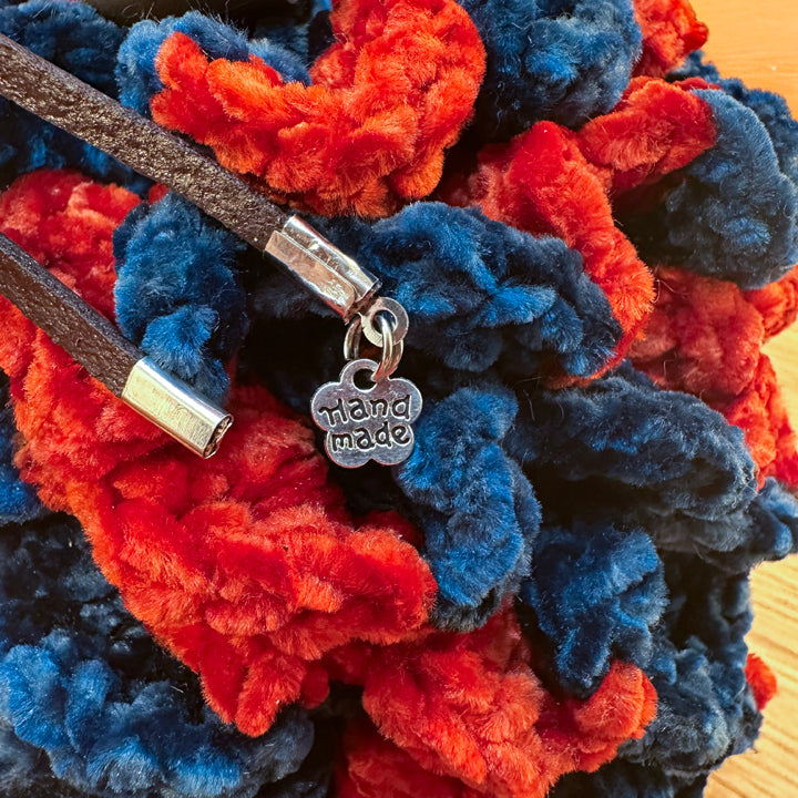 Close-up of navy and red crochet dragon egg dice bag with leather drawstring closure and metal ‘handmade’ tag.