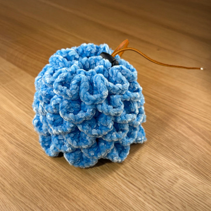 Crochet dragon egg dice bag made from sky blue velvet yarn with tan leather drawstring and black plastic toggle, shown closed.