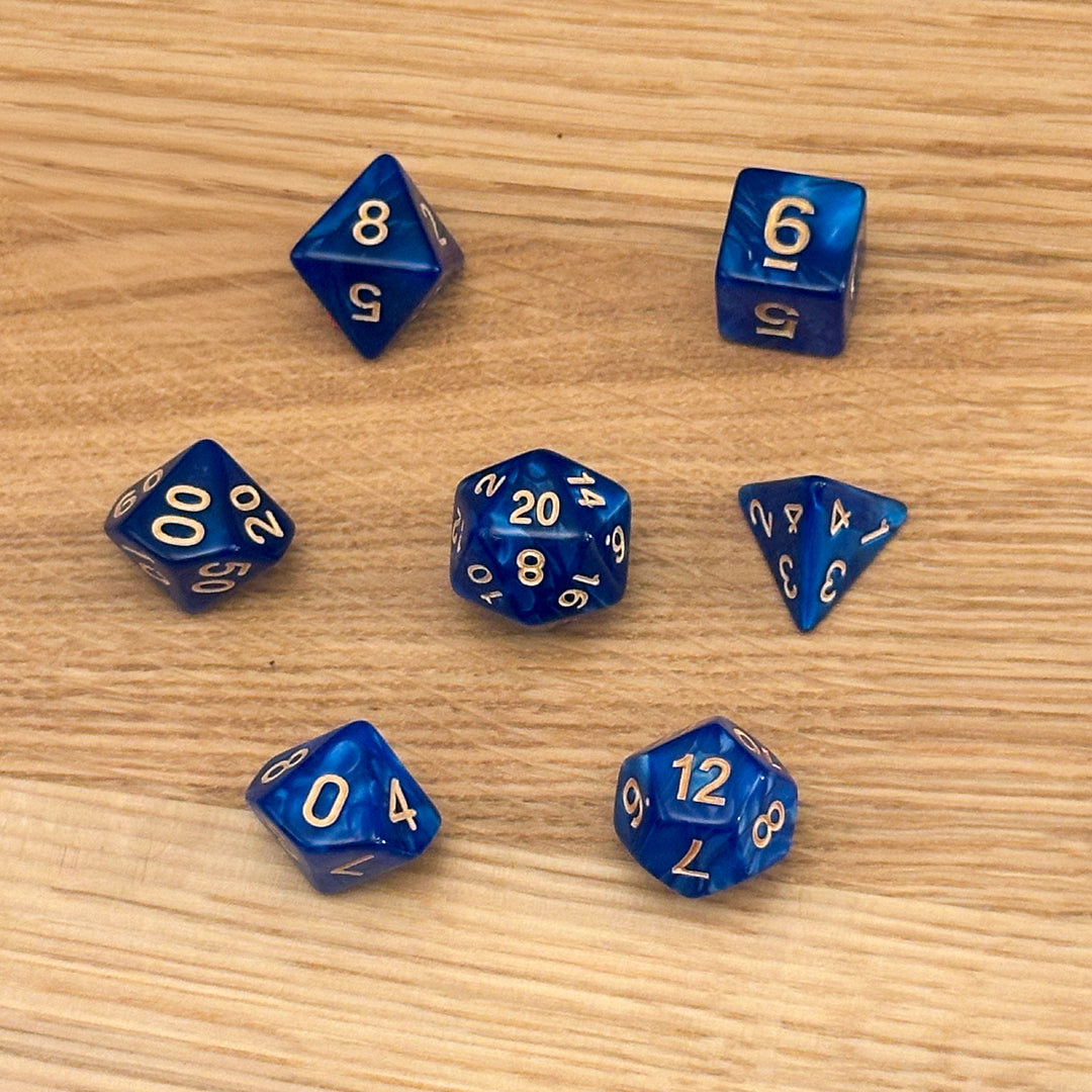 Set of 7 polyhedral dice (D4, D6, D8, D10, percentile D10, D12, D20) in swirled deep blue acrylic with gold number infill.