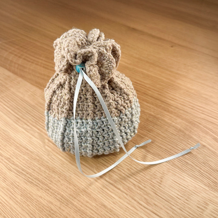 Closed tan and teal crochet dice bag with a teal glass bead closure. Part of the handmade hoard and fateweaver's collection.