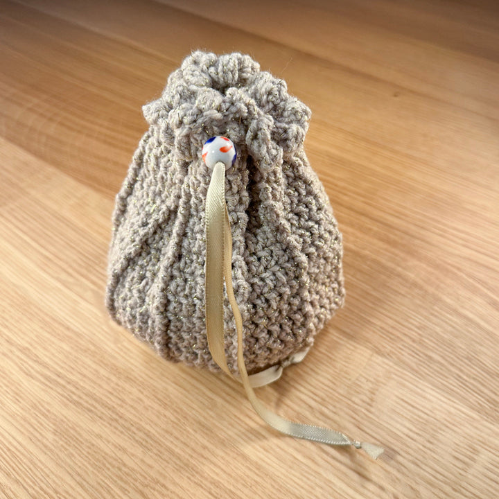 Closed tan crochet dice bag with a white glass bead closure. Part of the handmade hoard and fateweaver's collection.