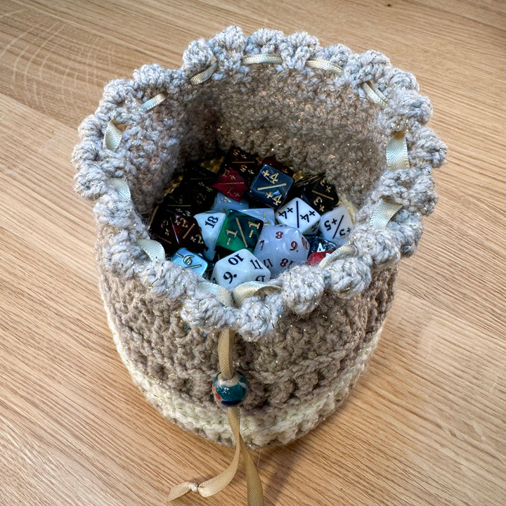 Tan and cream crochet pouch displayed open with 90 assorted dice inside to show capacity. Part of the handmade hoard and fateweaver's collection.