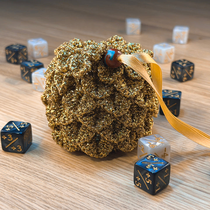 closed mini gold dragon egg crochet pouch, surrounded by MTG plus and minus dice. part of the handmade hoard and Fateweaver's collection