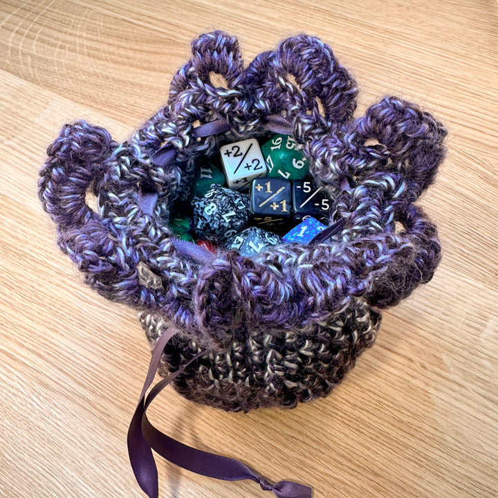 crochet pouch in purple and white yarn, displayed open with 90 assorted dice inside to show capacity. part of the handmade hoard and Fateweaver's collection