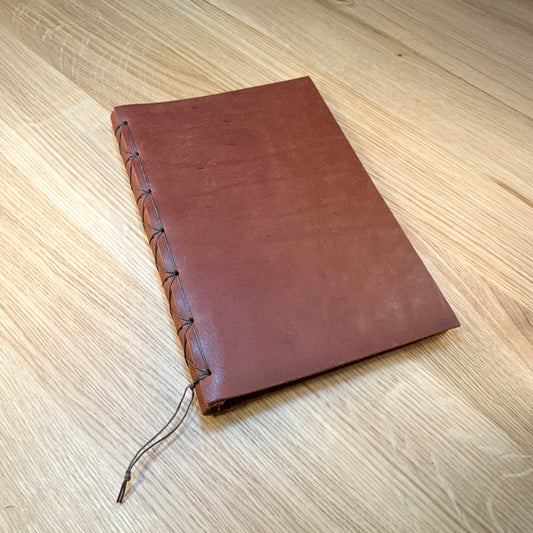 Closed journal with front cover showing chocolate vegetable-tanned leather and hand-stitched waxed thread binding along the spine.