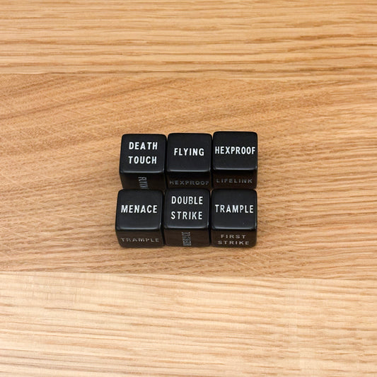 Six black keyword D6 with white infill, featuring keywords 'death touch', 'flying', hexproof', 'menace', 'double strike', and 'trample'.